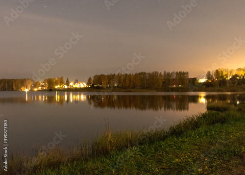 blurred wallpaper with lake at night, blurred lights on the horizon, lake reeds and grass in the foreground, autumn