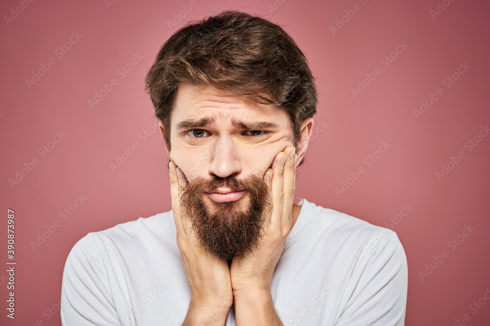 Emotional bearded man in white T-shirt discontent pink background