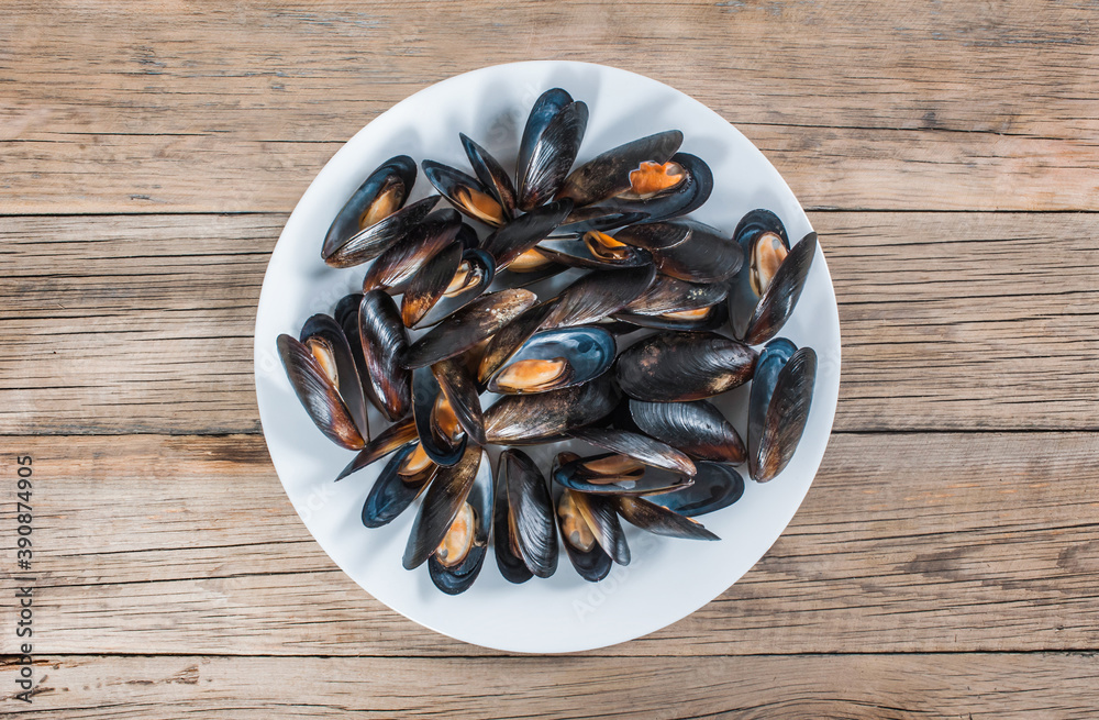 Many sea mussels in shells on a white plate on an old wooden background. View from above Many sea mussels in shells on a white plate on an old wooden background. View from above