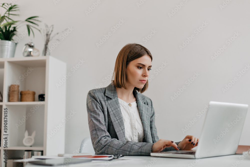 Attractive blonde woman typing letter in MacBook at her workplace. Photo of lady in stylish jacket in bright office Attractive blonde woman typing letter in MacBook at her workplace. Photo of lady in stylish jacket in bright office