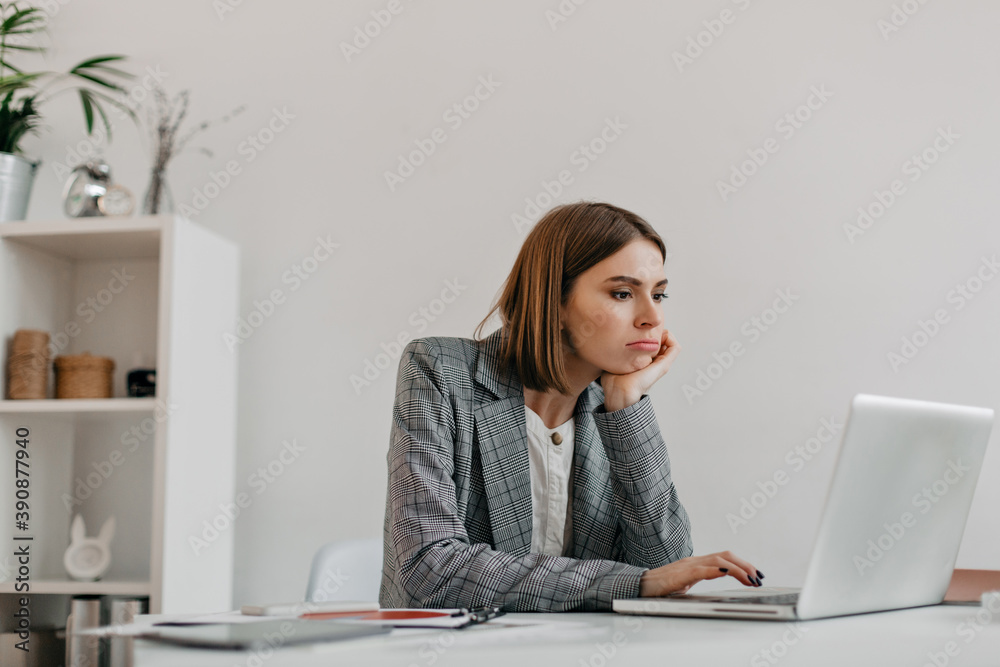 Bored young business lady in gray outfit looks at laptop screen at her workplace Bored young business lady in gray outfit looks at laptop screen at her workplace