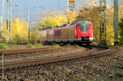 Gleisbett mit Gleisschotter und Schienenstrang und Nahverkehrszug auf freier Strecke in einer Kurve im Herbst - Stockfoto