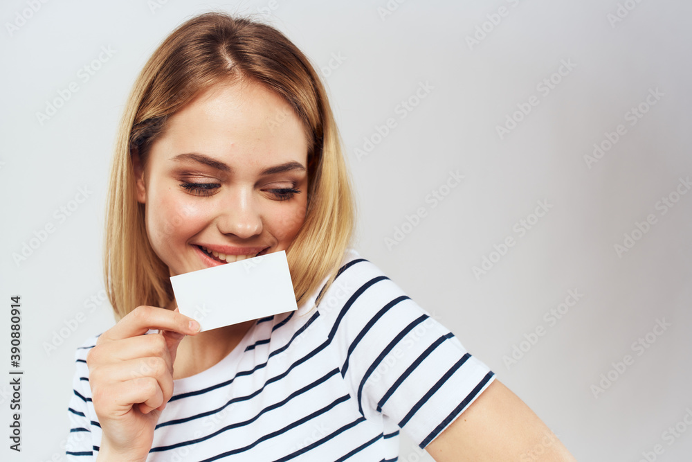 cheerful woman in a striped t-shirt holds a business card copy Space light background cheerful woman in a striped t-shirt holds a business card copy Space light background