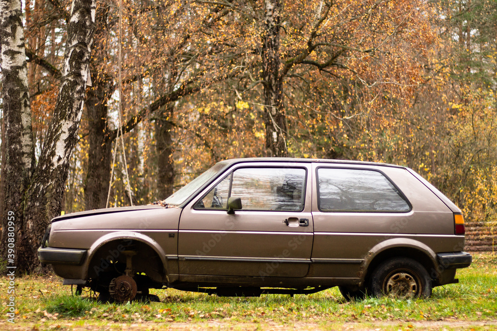 Old abandoned beige car without a wheel on the background of autumn nature