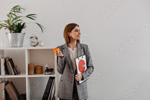Portrait of business woman with pie chart in her hands looking to side. Smiling woman is going to eat apple for lunch in office