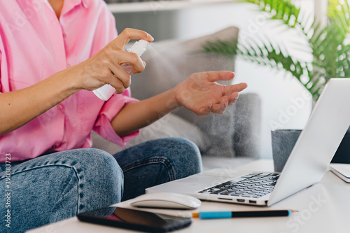 close up hands of woman spray sanitizer antiseptic at workplace at home working online on laptop