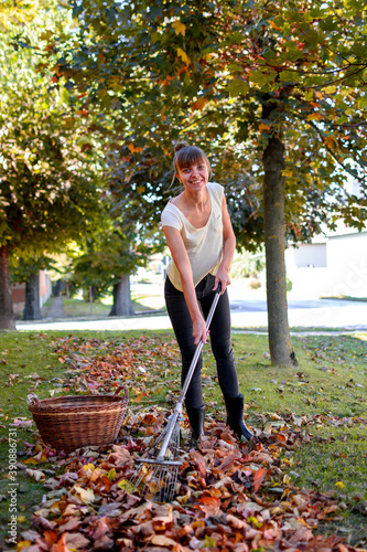Woman collecting leaves in front of house and smiling. She is holding rake next to wicker basket.