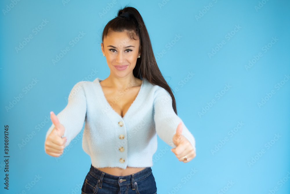 Smiling pretty young woman showing thumbs up isolated on the blue background Smiling pretty young woman showing thumbs up isolated on the blue background