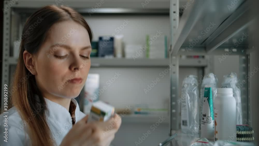 Beautiful woman checks the medicine goods in the drug store. Caucasian brown-haired woman rearranges cans and boxes with tablets on the storefront shelf and compares them to a list. Beautiful woman checks the medicine goods in the drug store. Caucasian brown-haired woman rearranges cans and boxes with tablets on the storefront shelf and compares them to a list.