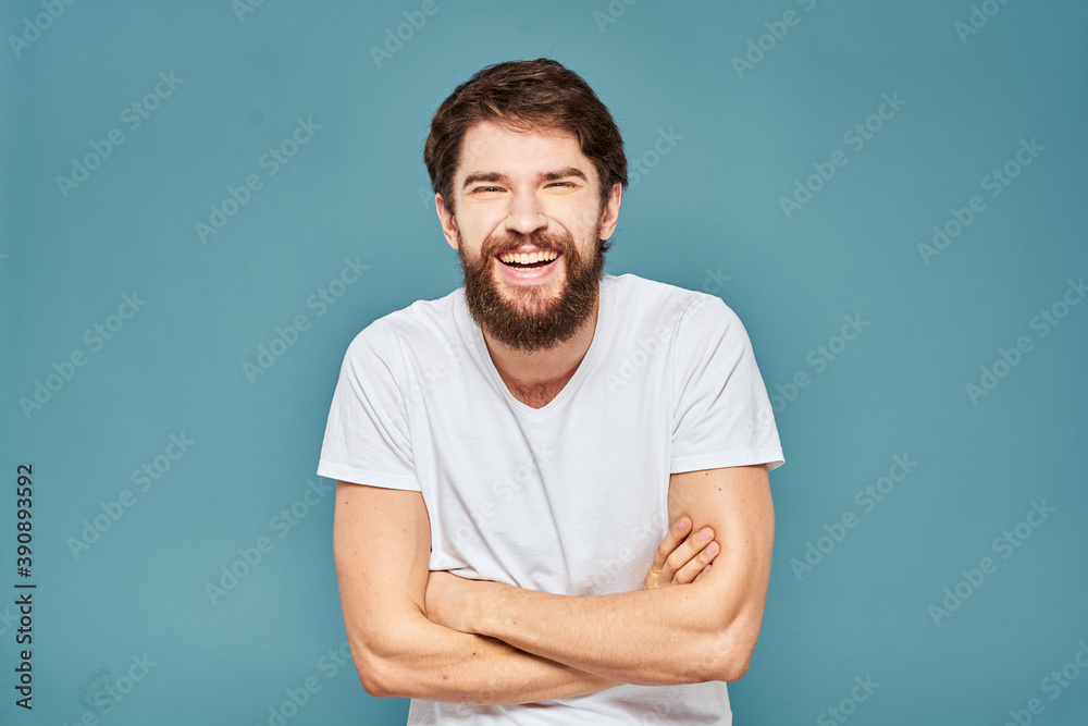 A bearded man in a white T-shirt gestures with his hands emotions blue background A bearded man in a white T-shirt gestures with his hands emotions blue background