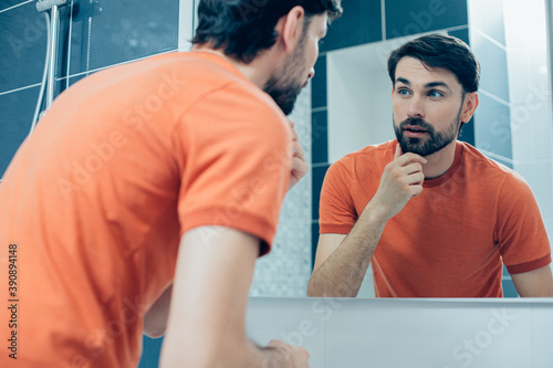 Handsome man looking at his reflection while being at home