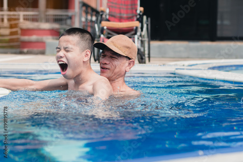 Strong arm muscles of Asian special child on wheelchair with swimming pool background,The boy happiness in holidays with family time on the travel,Lifestyle of happy disabled kid sport travel concept.