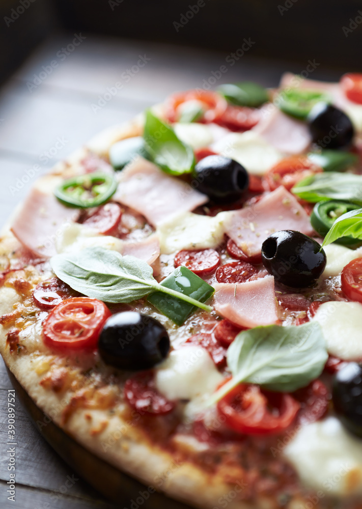Pizza with ham, mozzarella cheese, cherry tomatoes, green and jalapeno pepper, black olives and fresh basil. Dark background. Close up. 