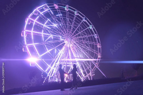 young man and woman romance love in the night in amusement park near ferris wheel