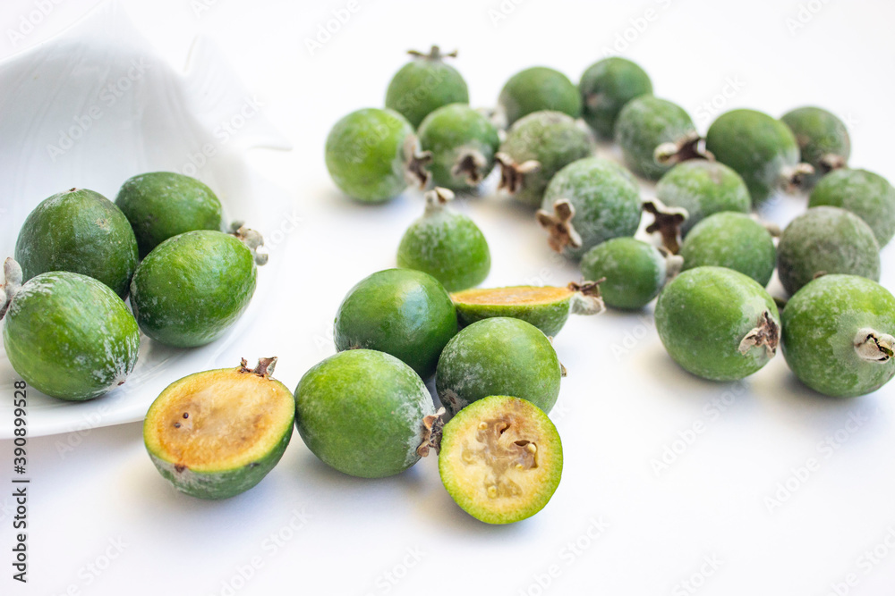 Large fleshy juicy Feijoa berries. Ripe dark green with sepals. A scattering of fruit on a light table and a white Cup. Whole and cut slices. Large fleshy juicy Feijoa berries. Ripe dark green with sepals. A scattering of fruit on a light table and a white Cup. Whole and cut slices.