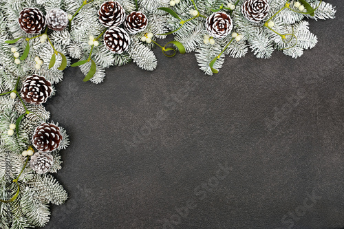 Fototapeta Naklejka Na Ścianę i Meble -  Winter snow covered spruce fir background border with pine cones & mistletoe on grey grunge. Frame design  for the solstice, Christmas & New Year festive season. Top view, flat lay, copy space.
