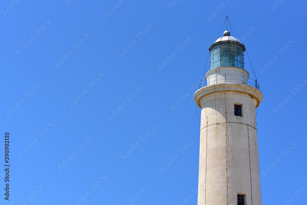 Close up of the top of a lighthouse, to the side of the picture, against a blue sky