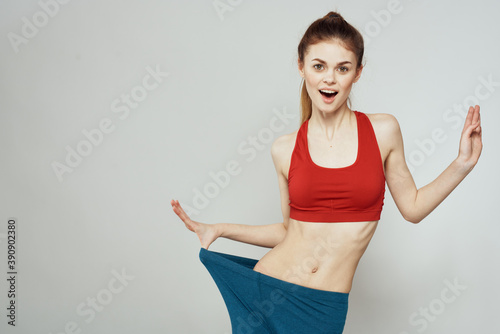 A woman in a red T-shirt on a light background is engaged in fitness gestures with her hands a slim figure 