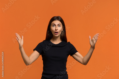 Wow how is big it. Happy emotional caucasian woman in black t-shirt shows huge gesture, measures something big, shouts loudly, shocked of gift size. Isolated over an orange background