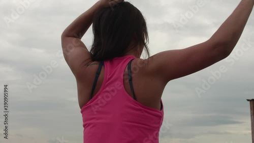 Back view of woman in pink tank doint exercises for upper part of back with fitness stretch band. photo