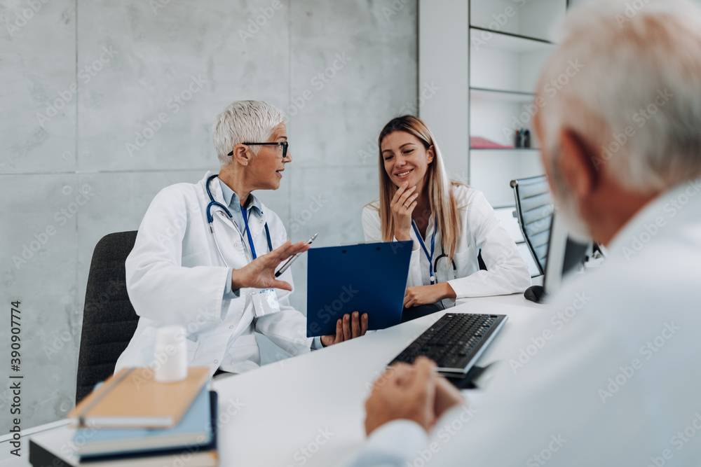 Doctors and senior male patient discussing something while sitting at the table in the doctor's office. Medicine and healthcare concept. Doctors and senior male patient discussing something while sitting at the table in the doctor's office. Medicine and healthcare concept.