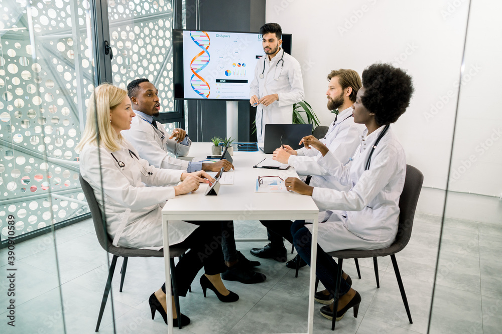 Fototapeta premium International medical team sitting and discussing at the table in the modern office. Young Indian doctor scientist having speech about clinical trials, chromosome deseases and gene engineering