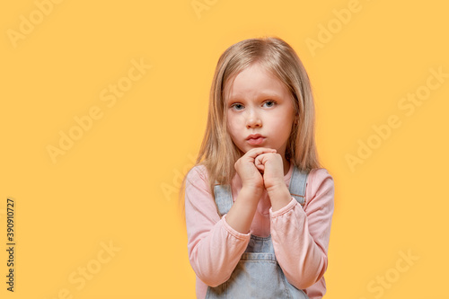 Cute beautiful blonde girl looks at the camera and pray. Yellow isolated background