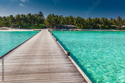 Jetty over atoll and a tropical resort island in Maldives