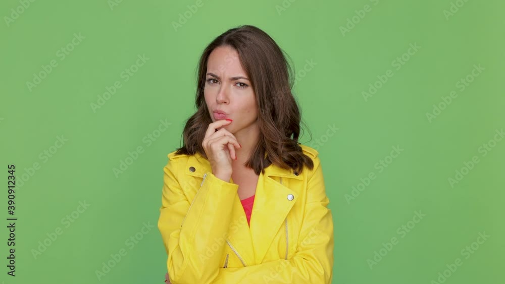 Puzzled pensive young brunette woman 20s years old in casual yellow leather jacket posing isolated on green background in studio. People lifestyle concept. Looking aside up put hand prop up on chin Puzzled pensive young brunette woman 20s years old in casual yellow leather jacket posing isolated on green background in studio. People lifestyle concept. Looking aside up put hand prop up on chin