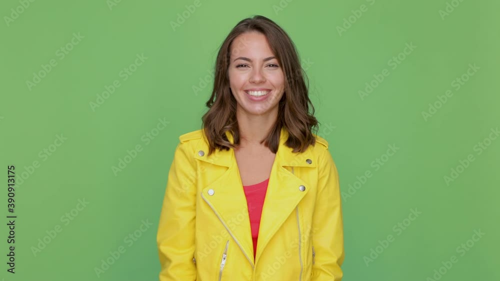 Funny young woman 20s years old in yellow leather jacket isolated on green background studio. People lifestyle concept. Point index fingers o camera doing phone gesture like says call me back blinking