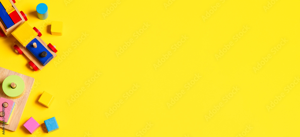 Baby kids toys banner background. Wooden train, educational stacking color recognition puzzle toy and colorful blocks on yellow background. Top view Baby kids toys banner background. Wooden train, educational stacking color recognition puzzle toy and colorful blocks on yellow background. Top view