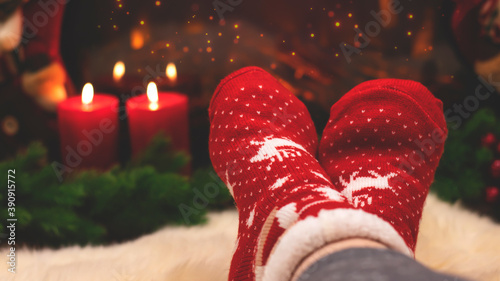 Red knitted socks against the background of New Year's decorations and fireplace, Christmas tree garland. Cozy winter evening by the fireplace, blurred background. New Year and Christmas festive backg