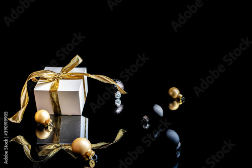 Happy new year. White gift with golden bow, gold balls and new year tree in Christmas decoration on dark background for greeting card. Winter festive composition with copy space.