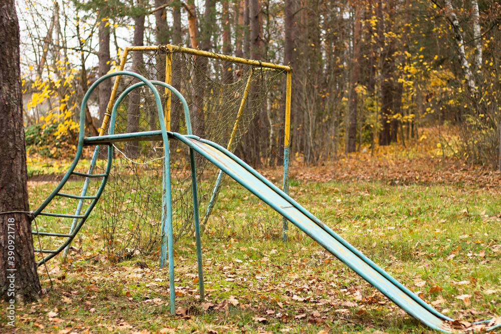 Abandoned playground in autumn. An old football goal with a torn net and a children's slide. Abandoned playground in autumn. An old football goal with a torn net and a children's slide.