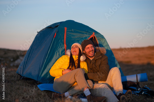 Happy smiling couple camping in front of a tent in the mountains at the sunset.