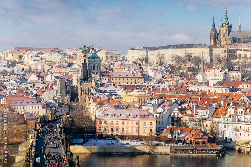 Aerial panoramic view from Old Town Bridge Tower, Karlov or Charles bridge and Vltava River in winter, sunny day, snow lies on red tiled roofs, Prague, Czech Republic