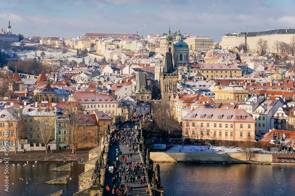Aerial panoramic view from Old Town Bridge Tower, Karlov or Charles bridge and Vltava River in winter, sunny day, snow lies on red tiled roofs, Prague, Czech Republic
