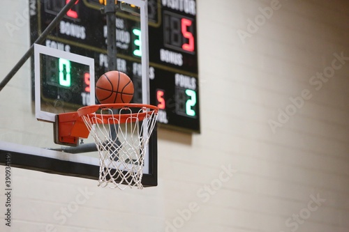 Basketball at the hoop with black scoreboard in background 