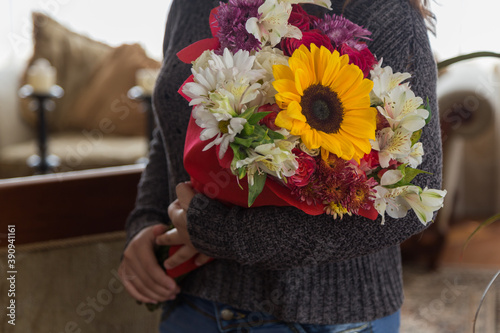 person holding beautiful and colorful bouquet of flowers with a sunflower and different kinds of flowers, in a room, gift of love