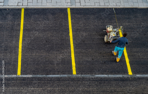 A worker is drawing outdoor concrete car parking lot is divided for making a slot for the park each car by a yellow line, with cement wheel coverings. in urban city.