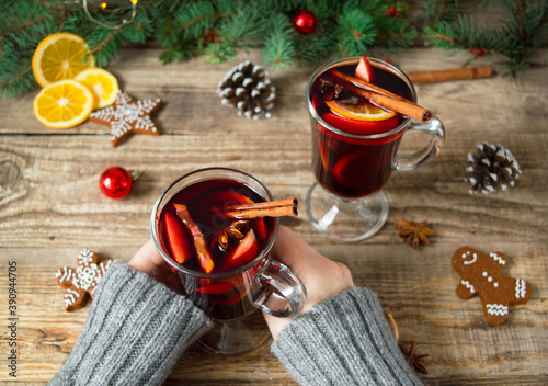 Top view of women holding glasses with Christmas hot mulled wine red with spices on a wooden background with fir branches and Christmas decor. New year's drinks.Traditional hot drink .