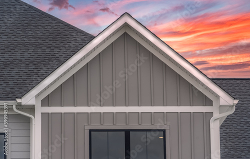 White frame gutter guard system, with dark gray horizontal vinyl siding, white accents, fascia, soffit, on a pitched roof attic at a luxury American single family home dramatic colorful sunset sky photo