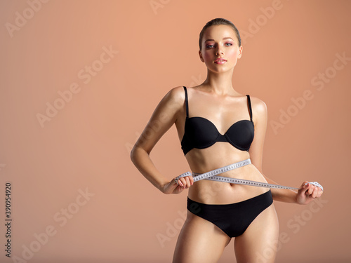 Young woman with tape and a beautiful, healthy body. Sexy woman measuring her perfect body.