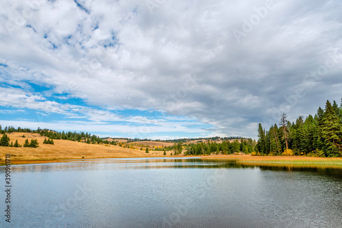 Lake near yellow hills and green forest on a sunny autumn day