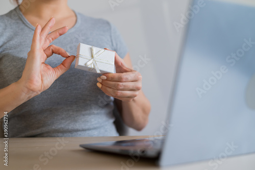 Online sale of gifts. A woman is holding a gift box in front of a laptop