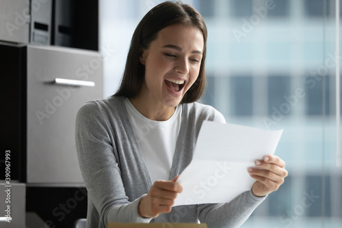 That is amazing. Overjoyed laughing young lady office manager employee reading formal paper message confirming full payment of credit loan, informing that her project research becoming grant recipient