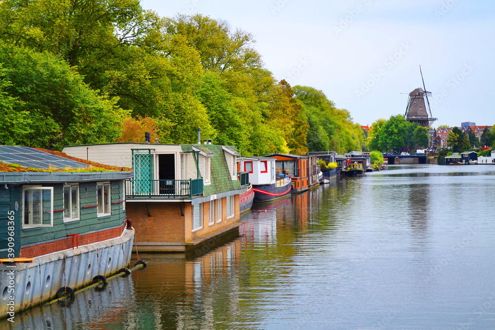 Fototapeta premium Amstel river with houseboats in Amsterdam city, The Netherlands. Windmill in a background.