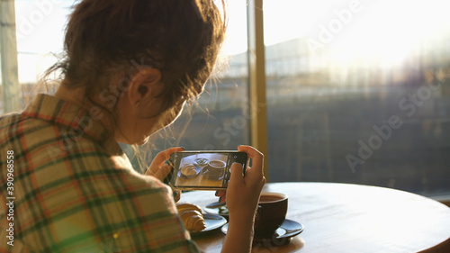 Close up of woman holds modern smartphone and taking pictures of her morning breakfast coffee and tasty croissant buns to share photos on social media resources