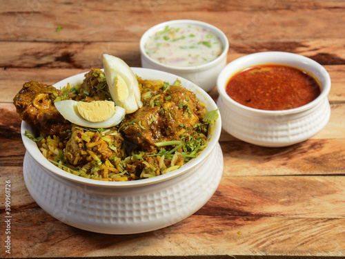 Traditional Hyderabadi Chicken dum Biryani made of Basmati rice cooked with masala spices, served with Onion raita and Salan, selective focus