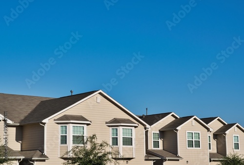 Townhome rooftops in the suburbs joined together tapering off into the distance under a clear blue sky with copy space above. © Brett